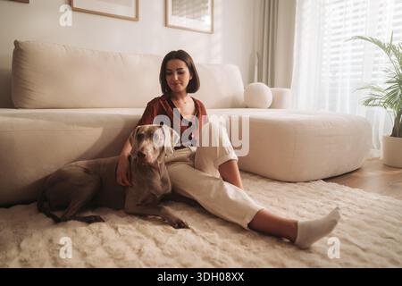 Frau und Hund in ruhigem Raum, ruhige Szene von Frau und Hund, die sich zu Hause im sanften Morgenlicht sonnen Stockfoto