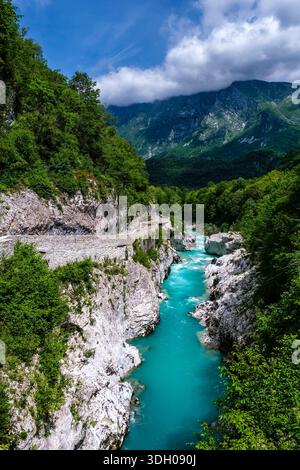 Hoher Blick auf den türkisfarbenen Soca Fluss, der durch eine felsige Schlucht fließt, mit steilen Bergen unter Wolken in der Ferne. Stockfoto