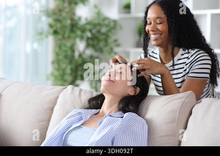 Glückliche schwarze Frau, die zu Hause einer asiatischen Freundin Kopfmassage macht Stockfoto