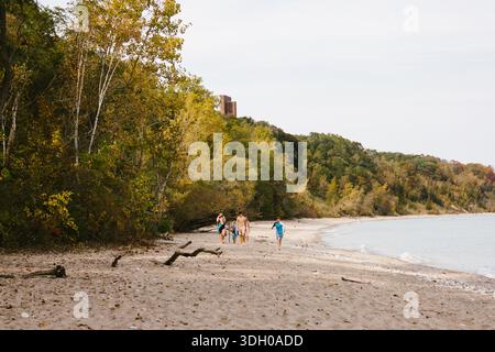 Eine Gruppe von Kindern spaziert entlang des von Bäumen gesäumten Strandes am See Stockfoto