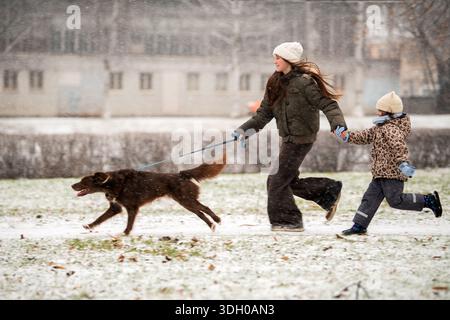 Zwei Schwestern laufen mit ihrem braunen Hund im Winter im Schnee. Stockfoto
