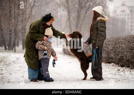 Mutter und Töchter unterschiedlichen Alters spielen mit Hund im verschneiten Park Stockfoto