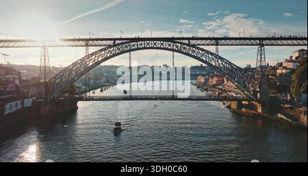 Portugal, Porto: Brücke Dom Luis I, die bei Sonnenuntergang den Fluss Douro überspannt, moderne Gebäude entlang des Flusses und ein Boot, das darunter gleitet, zeigt urbanes Zitat Stockfoto