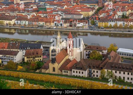 Erhöhter Blick auf eine historische Kirche mit zwei Türmen mit Blick auf Weinberge, den Main und die dichte Stadtentwicklung in Würzburg. Stockfoto