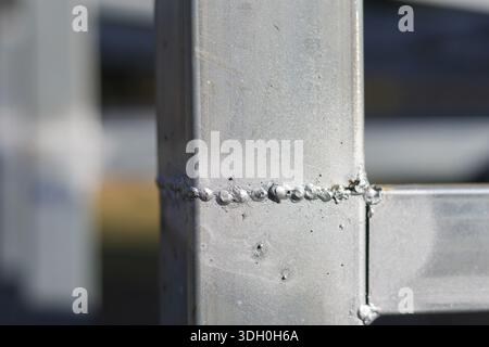 Großansicht eines robusten silbernen Metallrahmens mit rauer Schweißnaht, der industrielle Textur und Konstruktionsdetails in einem selbstbewussten, starken Stil unter hellem Licht zeigt Stockfoto
