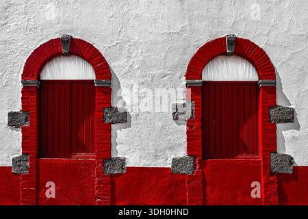 Scharlachrote Bogenfenster in einem alten Gebäude, an einer weißen Wand, Holzläden. Santiago Tianguistenco, mexikanischer Bundesstaat Mexiko Stockfoto