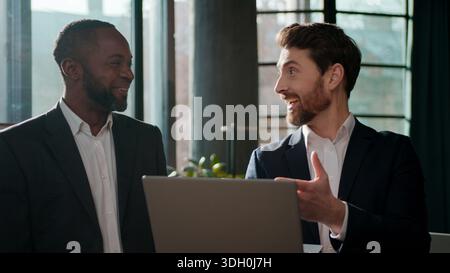 Fröhliches multiethnisches Business-Team mit Laptop sorglos positive Kollegen Geschäftsleute zwei Männer mit Computer im Büro emotional Happy Talking Stockfoto