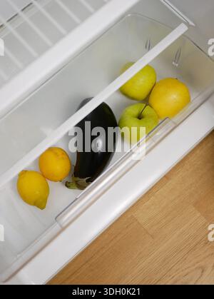 Blick von oben auf die minimale Kühlschublade mit frischem Obst und Gemüse. Äpfel, Zitronen und Auberginen im Kühlschrank. Das Konzept der gesunden Ernährung, Nutri Stockfoto