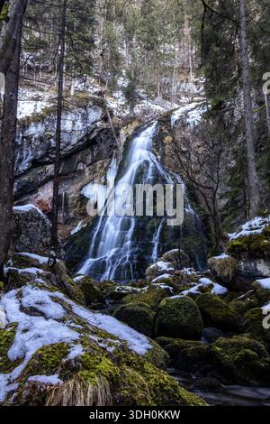 Ein atemberaubender Blick auf den Gollinger Wasserfall in Jänner, Österreich, im Winter. Der Wasserfall stürzt moosbedeckte Felsen hinunter, die teilweise mit Eis gefroren sind Stockfoto