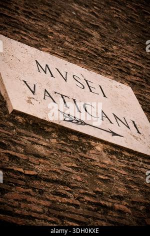 Marmorschild an einer alten Backsteinmauer, das auf das Musei Vaticani (Vatikanische Museen) mit einem eingravierten Pfeil, Vatikanstadt, zeigt. Stockfoto
