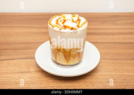 Ein hohes, zylindrisches Glas, gefüllt mit kristallklarem Eis, über das langsam dunkler Kaffee gegossen wird, vermischt mit großzügigen Bändern aus zähflüssigen, goldenen Ca Stockfoto