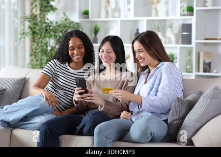 Drei glückliche Freunde, die online mit Kreditkarte und Telefon zu Hause bezahlen Stockfoto