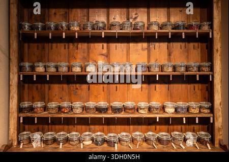 Viele pflanzliche Zutaten werden in den kleinen Vakuumgläsern mit dem Namensschild auf dem Holzregal aufbewahrt. Stockfoto