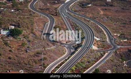 Teneriffa, Kanarische Inseln: Aus der Vogelperspektive gewundene Autobahnstraßen mit Autoverkehr durch die Vulkanlandschaft Teneriffas, Spanien, wodurch ein Netz von Verkehrswegen entsteht. Drohnenflug Stockfoto