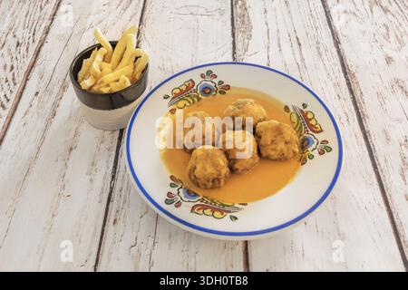 Mehrere kleine Fleischbällchen, wie sie für Tapas verwendet wurden, mit Zahnstochern aufgespießt und in einer roten Sauce in einer kleinen Töpferauflaufform eingetaucht Stockfoto