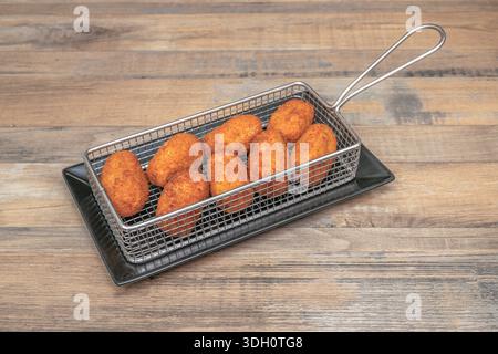 Geriebene Rinderkroketten mit deutlich sichtbaren Fleischsträngen im Inneren, serviert auf einem Teller mit gerösteter roter Pfeffersauce. Stockfoto