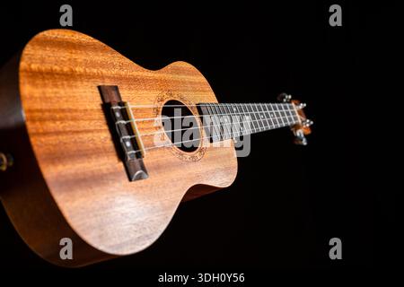 Eine klassische braune Akustikukulele mit weißen Holzsaiten und schwarzem Hintergrund, wie ein Volksmusikinstrument, bereit für Jazz- und Rock-Conce Stockfoto