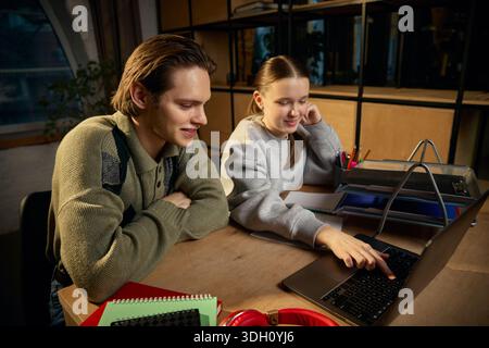 Schwester, die auf einem Laptop studiert, mit Bruder-Unterstützung zu Hause. Stockfoto
