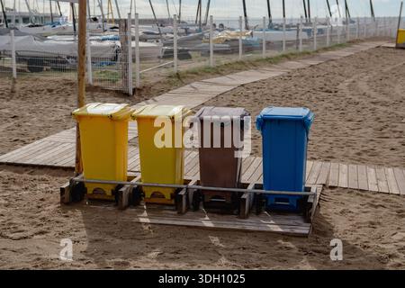 Vier farbenfrohe Recyclingbehälter am Strand zur separaten Abfallsammlung. Umweltkonzept zur Förderung von Recycling, Sauberkeit und ökologischem Handeln Stockfoto
