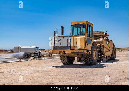 Seitenansicht des großen gelben Traktors. Die Bewässerungsmaschine bewässert die Straße. Autobahnbau. Stockfoto