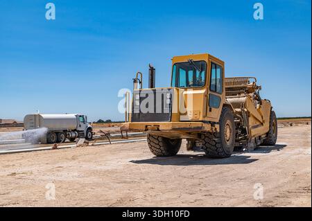 Seitenansicht des großen gelben Traktors. Die Bewässerungsmaschine bewässert die Straße. Autobahnbau. Stockfoto