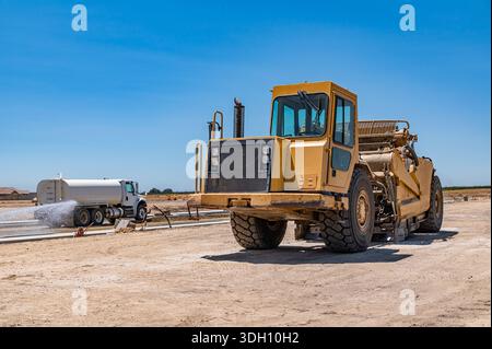 Seitenansicht des großen gelben Traktors. Die Bewässerungsmaschine bewässert die Straße. Autobahnbau. Stockfoto