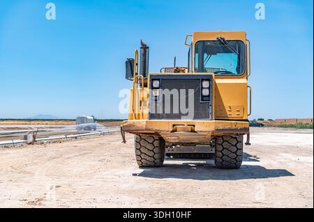 Gelber Traktor, Straßenreparatur. Nahaufnahme. Bewässerungsmaschine im Hintergrund. Stockfoto