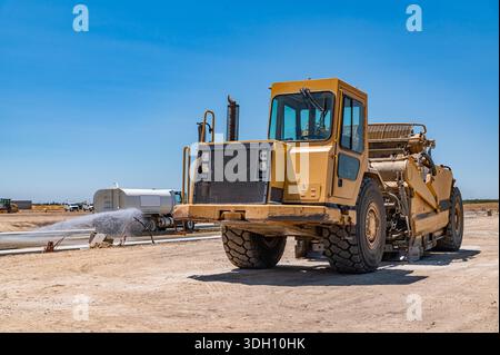 Seitenansicht des großen gelben Traktors. Die Bewässerungsmaschine bewässert die Straße. Autobahnbau. Stockfoto