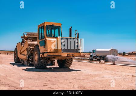 Seitenansicht des großen gelben Traktors. Die Bewässerungsmaschine bewässert die Straße. Autobahnbau. Stockfoto