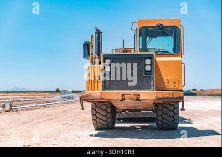 Gelber Traktor, Straßenreparatur. Nahaufnahme. Bewässerungsmaschine im Hintergrund. Stockfoto