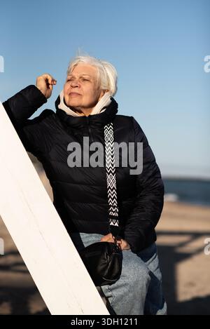 Eine ältere Frau, die an einem sonnigen Tag am Strand in der Nähe des Meeres steht Stockfoto