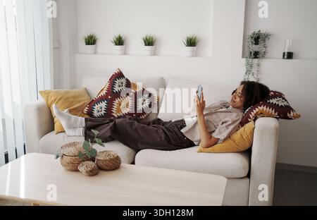 Eine Frau Lag Bequem Auf Dem Sofa, Eine Ruhige Dame Lehnte Sich Auf Der Couch, Während Sie Durch Ihr Gerät Scrollte Stockfoto