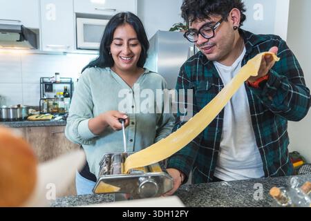 Glückliches Paar, das frische hausgemachte Pasta mit einer Nudelmaschine in ihrer modernen Küche zubereitet Stockfoto