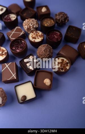Close-up-Flachbild mit verschiedenen handwerklichen Pralinen und Trüffeln auf einer Lavendelplatte, mit verschiedenen Texturen, Ganachefüllungen, Nuss- und Fruchtplatte Stockfoto