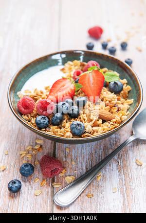 Müsli mit Joghurt, Erdbeeren, Heidelbeeren und Himbeeren in einer Keramikschale Stockfoto