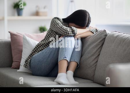 Aufgeregte junge Frau, die auf der Couch sitzt und weint Stockfoto