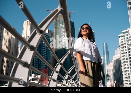 Junge Frau auf der Brücke in Dubai, flacher Blick auf die moderne Stadtarchitektur und Glasgebäude Stockfoto