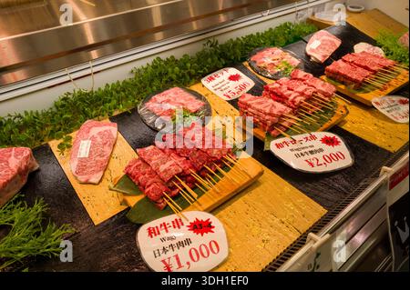 Osaka, Japan - 7. November 2023: Verschiedene Stücke von Wagyu-Rindfleisch, darunter Spieße und Steaks, werden auf Tabletts mit Preisschildern in japanischem Yen an einem Fleischstand im Kuromon Ichiba-Markt angeordnet. Stockfoto