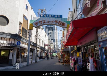 Osaka, Japan - 7. November 2023: Der Eingang zur South Road Sennichimae Shopping Street ist mit einem Schild über dem Kopf in japanischen Gebäuden, Geschäftsgebäuden, Ladenschildern, Bekleidungsdisplays und mehreren Fußgängern zu sehen, die bei Tageslicht die Straße entlang laufen. Stockfoto
