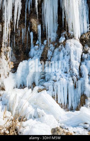 Atemberaubende lange blaue Eiszapfen hängen von einer felsigen Klippe an einem gefrorenen Wasserfall Stockfoto