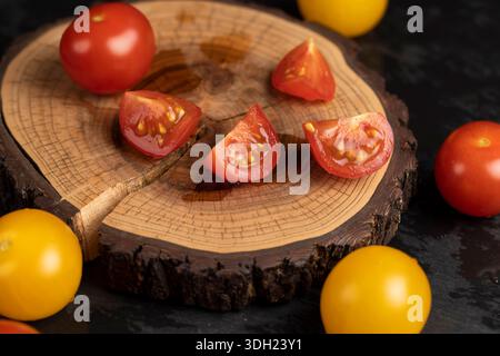 Eine in Stücke geschnittene rote Tomate und frische und reife Tomaten von roter und gelber Farbe auf dem Tisch, mehrere Tomaten liegen auf einem Holzbrett und einem Stockfoto