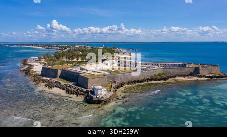 Die Festungsmauern aus der Vogelperspektive umschließen den Rand der Insel, während türkisfarbenes Wasser auf den historischen Stein trifft: Ilha de Mocambique, Nampula, Mosambik. Stockfoto