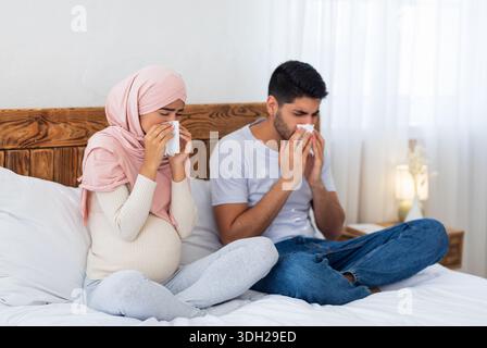 Das junge, schwanger-muslimische Paar bekam eine Grippe, hatte eine laufende Nase, saß zu Hause auf dem Bett und niesen in Papiergewebe Stockfoto