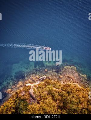 Aus der Vogelperspektive eines Bootes, das durch das tiefblaue Meer in der Nähe der zerklüfteten Küste von Northbridge, New South Wales, Australien fährt. Stockfoto