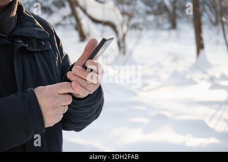 Nahaufnahme von Reifen erwachsenen Männerhänden mit Smartphone im Freien im Winter. Älterer Mann, der an kalten Tagen ein Mobiltelefon hält, Technologie und Kommunikation Stockfoto