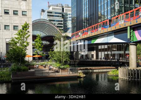 Ein Zug der Docklands Light Railway überquert den Eden Dock Park im Londoner West India Dock, umgeben von den Wolkenkratzern der Canary Wharf. Stockfoto