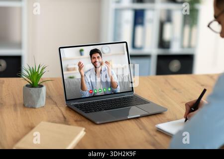 Junger Mann, der sich virtuell mit seinem arabischen Kollegen trifft und im Büro mit einem Laptop online kommuniziert Stockfoto