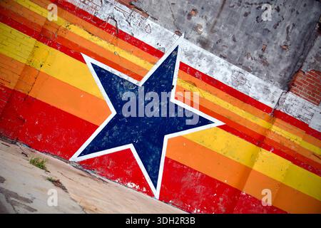 Städtisches Wandgemälde mit einem großen blauen Stern mit roten, orangefarbenen und gelben Streifen auf einer dicken Ziegelwand. Stockfoto