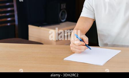 Nahaufnahme der Hand mit blauem Stift, beginnend mit dem Schreiben auf weißem Blatt über der Holzoberfläche. Stockfoto