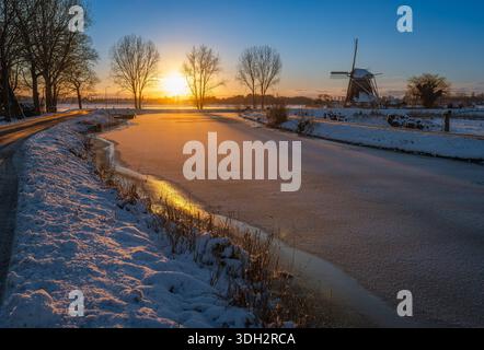 Niederländische Winterlandschaft mit historischer Windmühle in Abcoude und gefrorenem Fluss Gein bei Sonnenuntergang Stockfoto